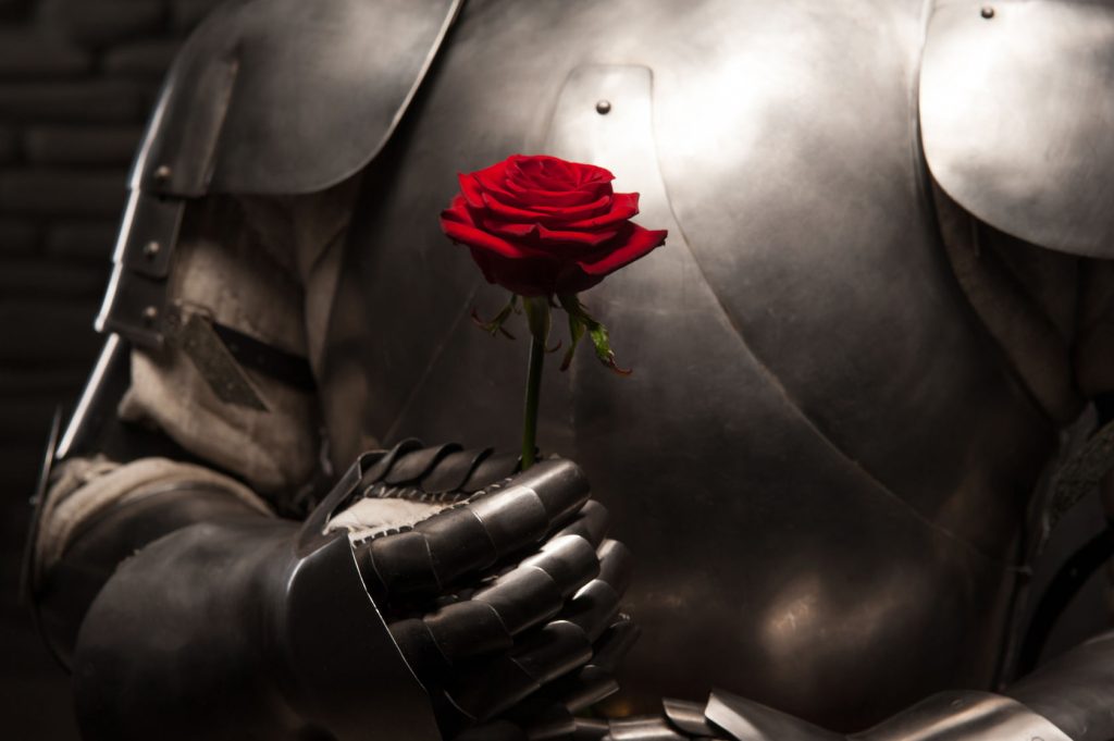 29700215 - closeup portrait of medieval knight in armor holding red rose on dark background, romance concept