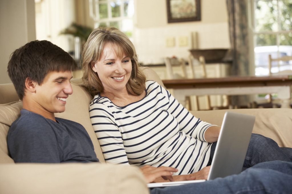 42269892 - mother with teenage son sitting on sofa at home using laptop