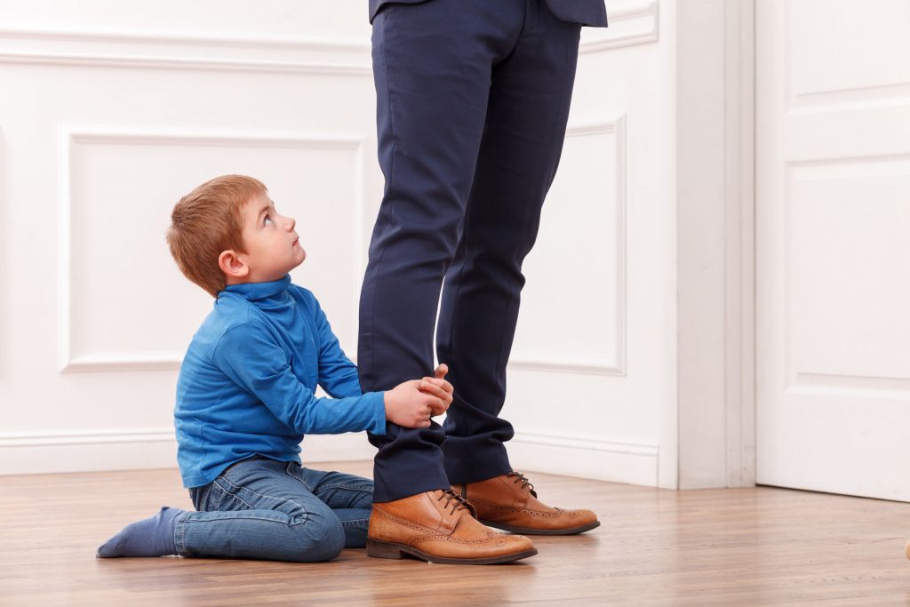 47922800 - close up of legs of man going to work. his son is asking him not to go. the child is sitting on flooring and gripping legs of his father. the boy is looking up with request