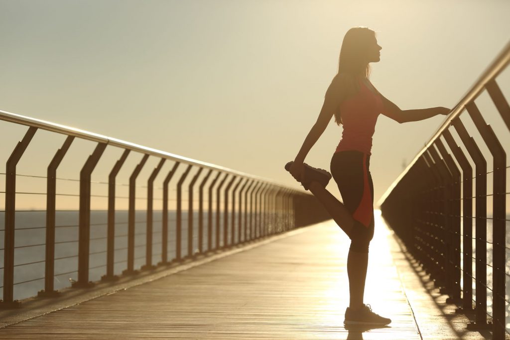 39083244 - woman silhouette exercising stretching on a bridge after running at sunset