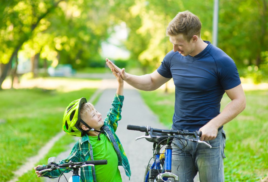 44519860 - father and son give high five while cycling in the park