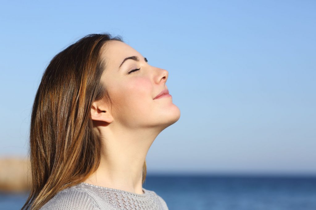 26781140 - woman profile portrait breathing deep fresh air on the beach with the ocean in the background