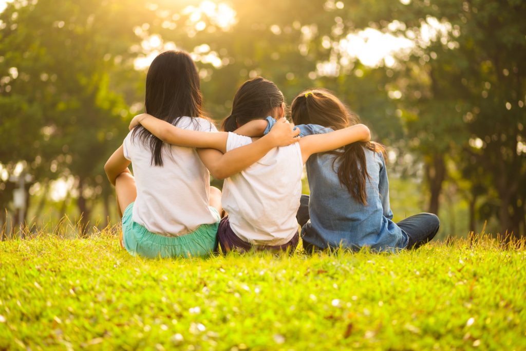 39554266 - back view of cute girls seated on green grass and relaxing