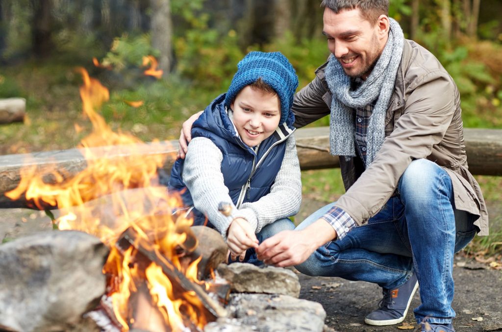 49276455 - camping, tourism, hike, family and people concept - happy father and son roasting marshmallow over campfire